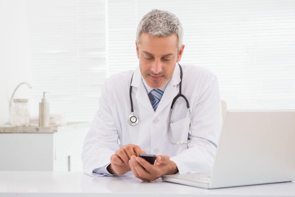 Smiling doctor touching his phone in medical office