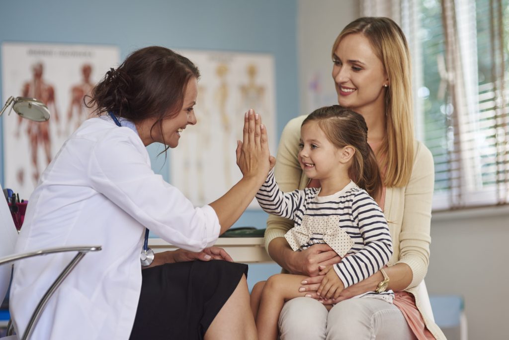 Female pediatrician high-fiving a girl sitting on her mom's lap