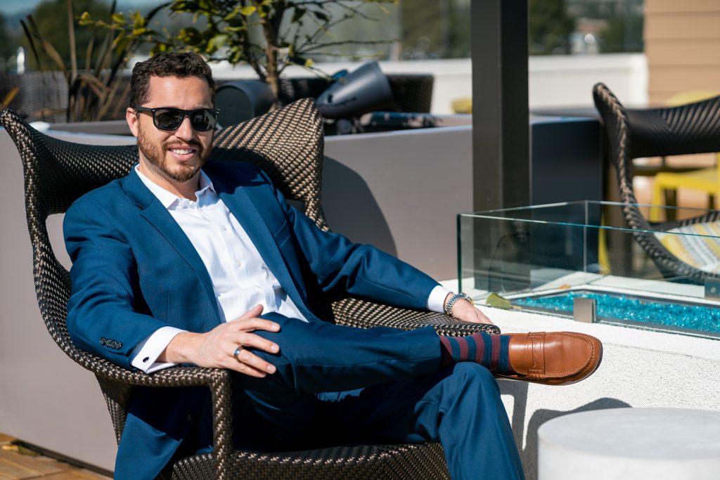 the author - white male sitting outside wearing sunglasses, blue suit, white shirt