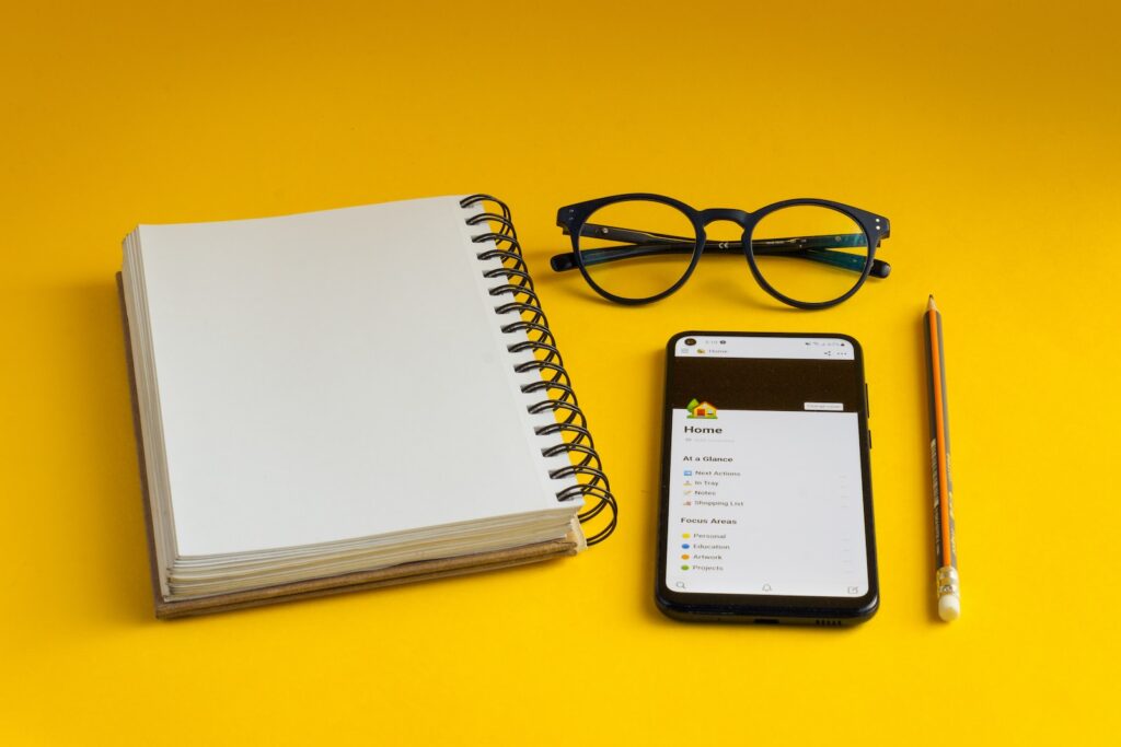 a notepad, glasses, pencil, and cell phone on a yellow surface